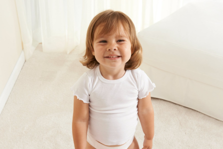 A Toddler in a white t-shirt standing and grinning.