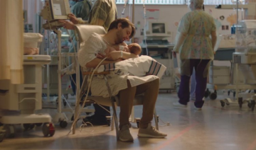 Parent sitting in the NICU giving hug and caressing the new born baby