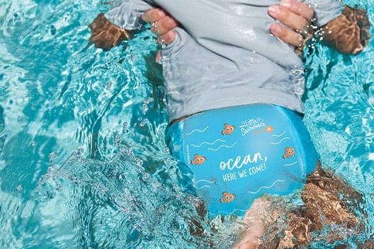 A parent holds their baby wearing a Huggies Little Swimmers Swim Pant with the Finding Nemo design while they splash in a pool