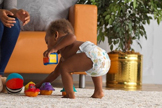 A diapered baby bends over to pick up toys from the floor