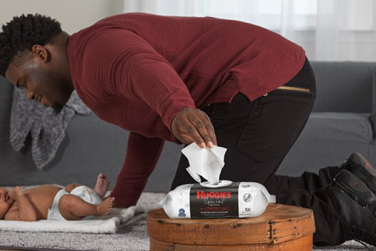 A father leans over his baby while demonstrating the Huggies Special Delivery Wipes' EZ Pull lid