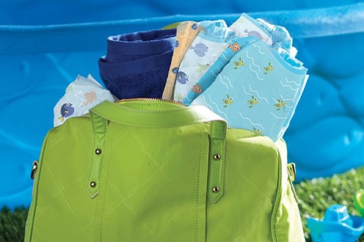 A green diaper bag full of Huggies Little Swimmers with assorted Finding Nemo designs sits by a baby pool