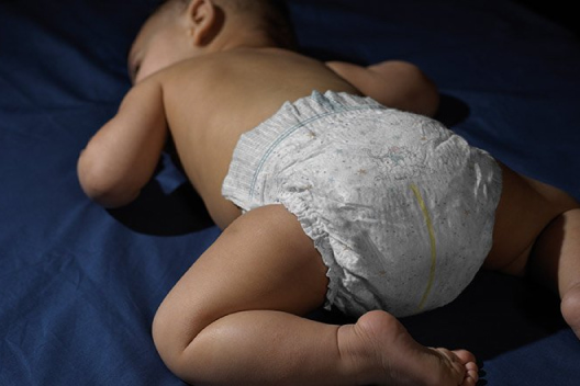 A baby sleeps on their tummy wearing a Huggies Overnites Diaper with extra absorbency