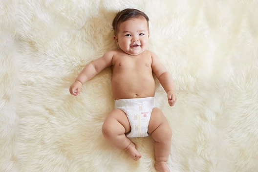 A diapered baby smiles while laying on a fuzzy off-white blanket