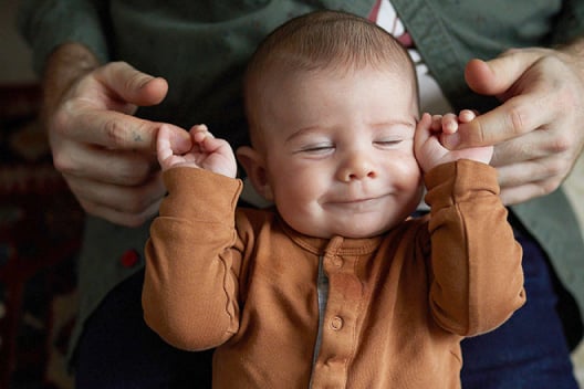 A smiling baby holds onto their father's index fingers