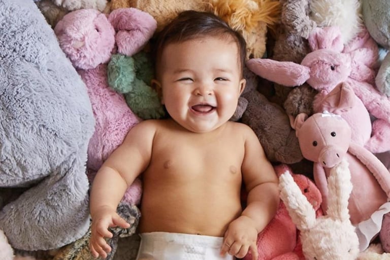 A laughing baby laying on a pile of stuffed animals
